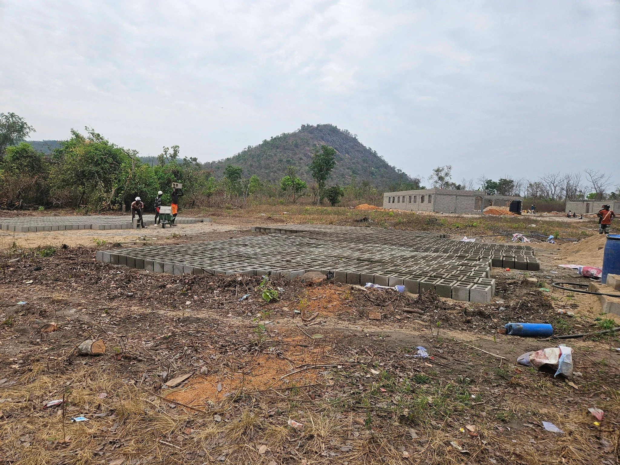  We always mold our own blocks on-site. Trucking them in is expensive, and causes too much damage to the blocks. You can see the school and teacher's quarters in the background, on the right. On the left, builders are laying the foundation for the clinic! 